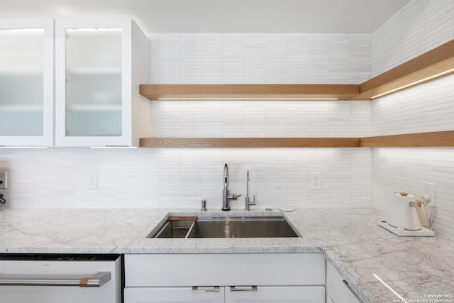 kitchen with a sink, white cabinetry, stainless steel dishwasher, decorative backsplash, and glass insert cabinets