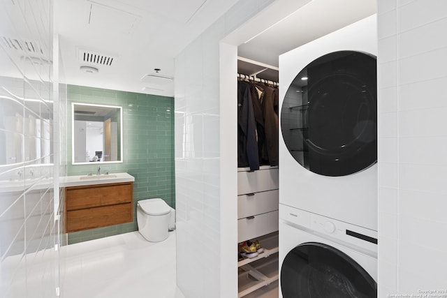 clothes washing area with laundry area, a sink, visible vents, tile walls, and stacked washer and clothes dryer