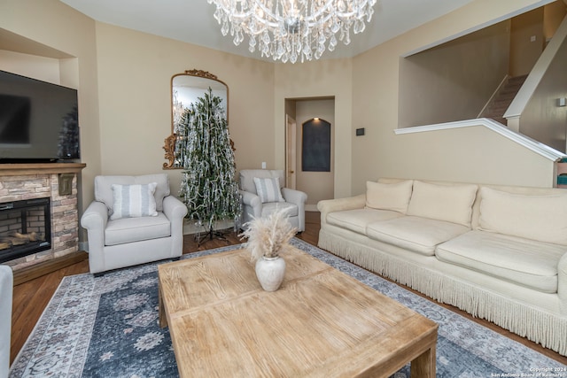 living room featuring a stone fireplace, wood-type flooring, and a chandelier