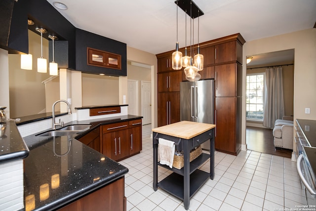 kitchen featuring sink, kitchen peninsula, dark stone countertops, pendant lighting, and high quality fridge