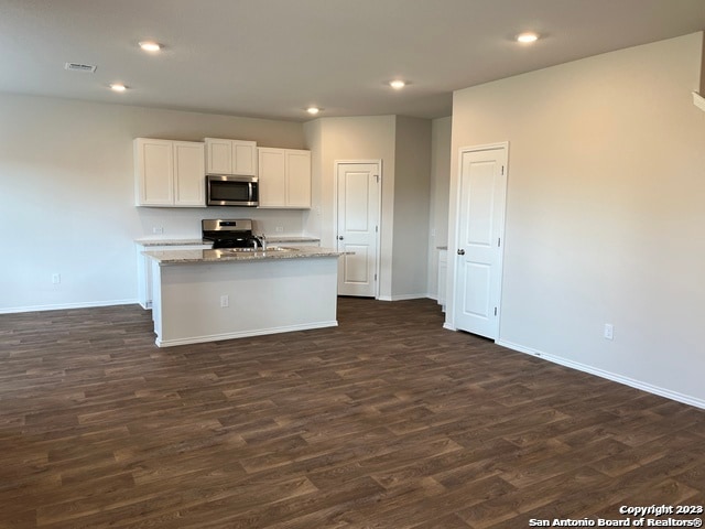 kitchen with dark wood-type flooring, an island with sink, appliances with stainless steel finishes, light stone counters, and white cabinetry