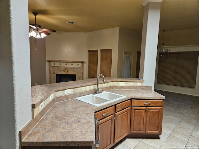 kitchen with a tile fireplace, ceiling fan with notable chandelier, sink, ornamental molding, and light tile patterned flooring