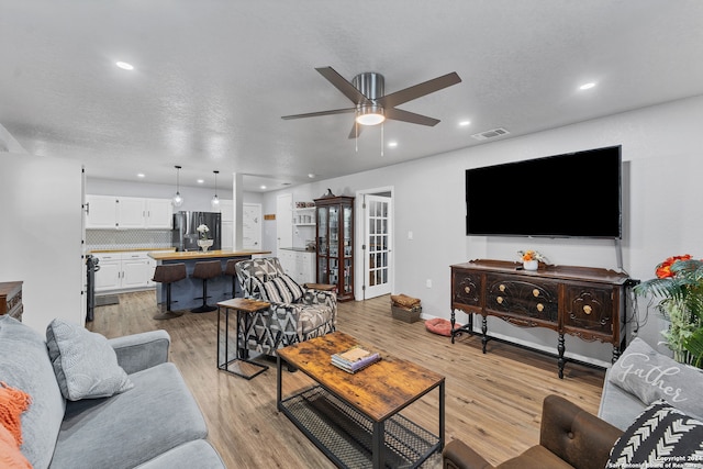 living room with ceiling fan, light hardwood / wood-style floors, and a textured ceiling