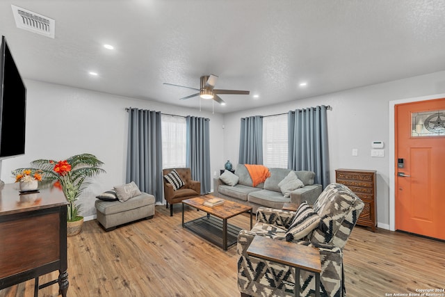 living room featuring ceiling fan, light hardwood / wood-style floors, and a textured ceiling