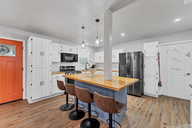 kitchen featuring light hardwood / wood-style flooring, decorative light fixtures, a breakfast bar, white cabinets, and appliances with stainless steel finishes