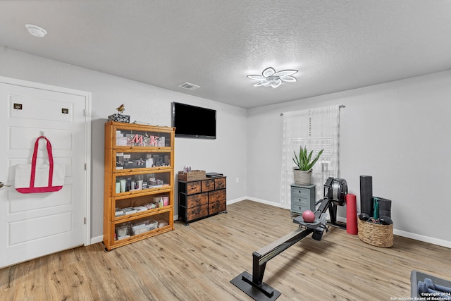 workout area with light wood-type flooring and a textured ceiling