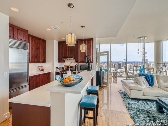 kitchen featuring a kitchen bar, backsplash, built in appliances, light hardwood / wood-style flooring, and hanging light fixtures