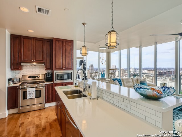 kitchen featuring appliances with stainless steel finishes, tasteful backsplash, sink, decorative light fixtures, and light hardwood / wood-style flooring