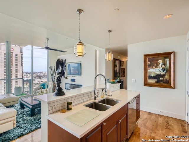 kitchen featuring ceiling fan, dishwasher, sink, hanging light fixtures, and light hardwood / wood-style floors