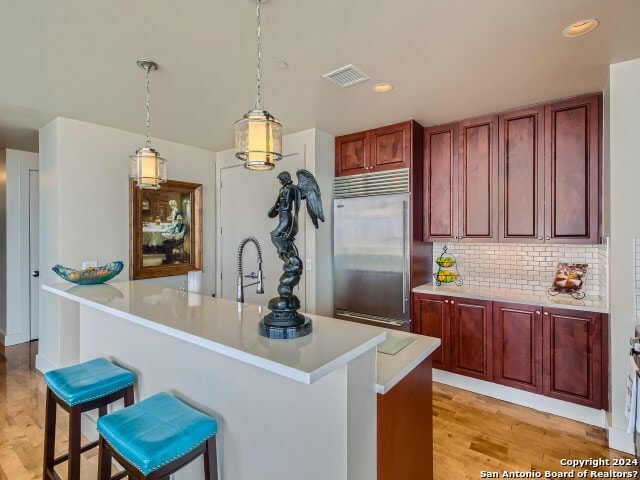 kitchen with sink, light hardwood / wood-style flooring, built in refrigerator, decorative light fixtures, and a breakfast bar area