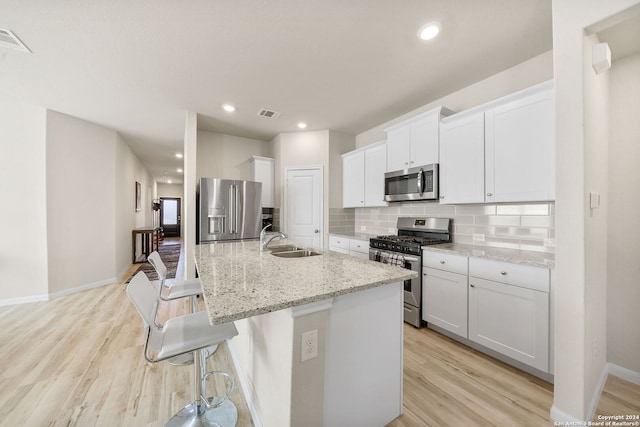 kitchen featuring a kitchen island with sink, white cabinets, sink, light hardwood / wood-style floors, and stainless steel appliances