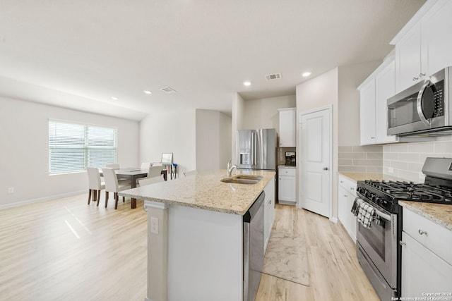 kitchen featuring light hardwood / wood-style flooring, an island with sink, appliances with stainless steel finishes, light stone counters, and white cabinetry