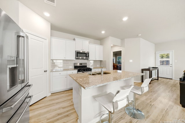 kitchen featuring a center island with sink, white cabinets, stainless steel appliances, and light hardwood / wood-style flooring