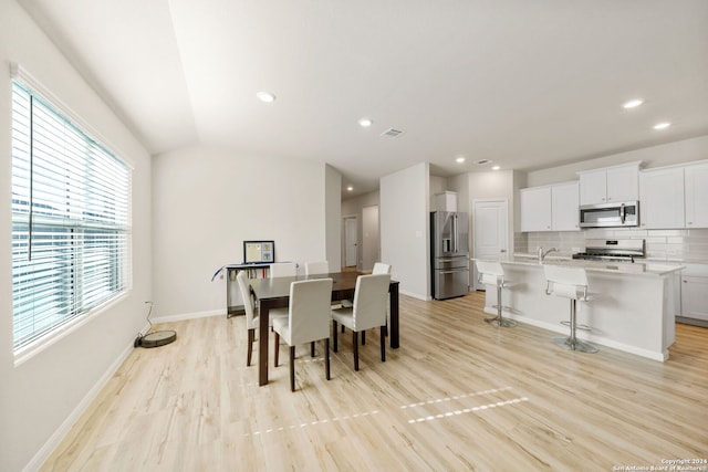 dining area with sink, light hardwood / wood-style floors, and vaulted ceiling