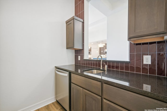 kitchen featuring sink, light hardwood / wood-style flooring, dark stone countertops, dishwasher, and backsplash