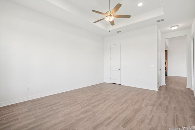 spare room with a raised ceiling, ceiling fan, and light wood-type flooring