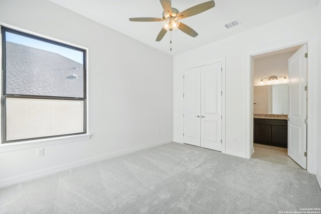 unfurnished bedroom featuring connected bathroom, light colored carpet, ceiling fan, and a closet