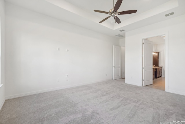 unfurnished room with a raised ceiling, light carpet, and ceiling fan