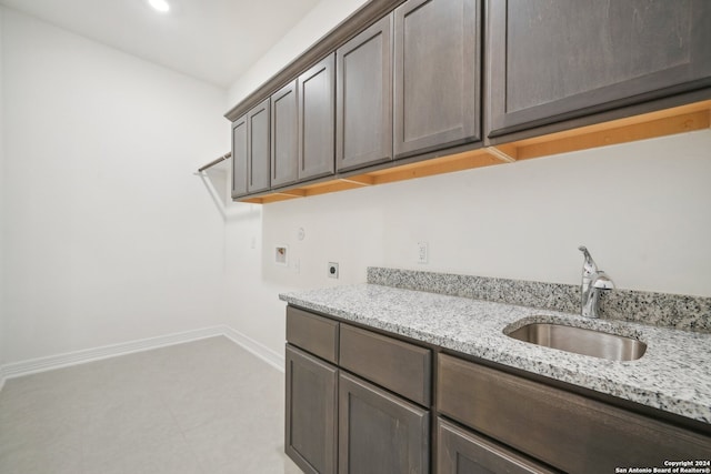 kitchen featuring dark brown cabinetry, sink, and light stone countertops