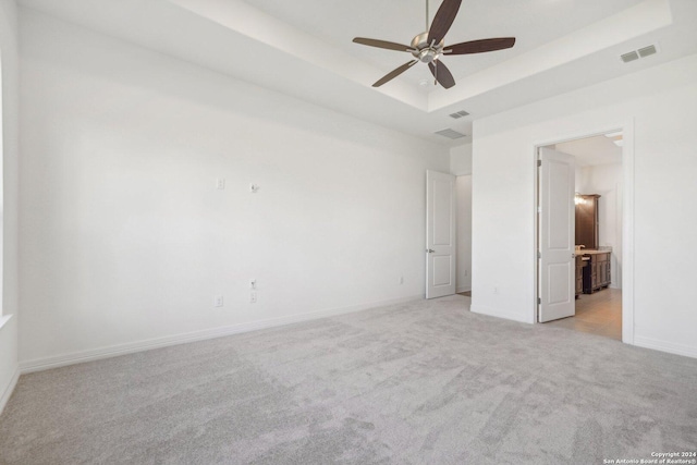 empty room with a raised ceiling, light colored carpet, and ceiling fan