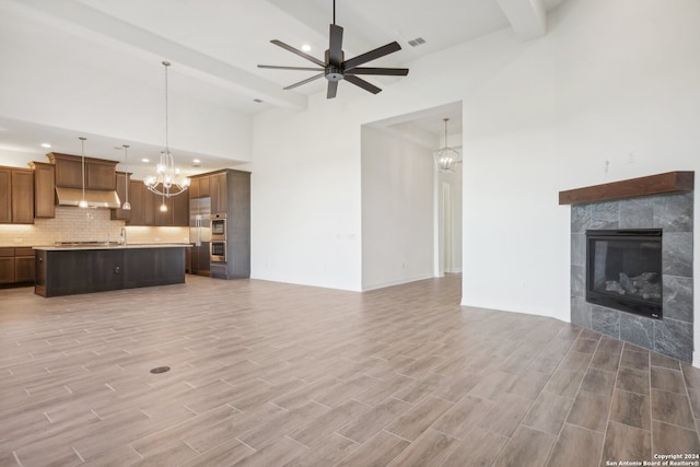 unfurnished living room with beamed ceiling, a tile fireplace, and ceiling fan with notable chandelier