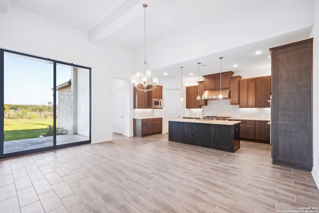 kitchen with pendant lighting, a kitchen island with sink, an inviting chandelier, stainless steel microwave, and beamed ceiling