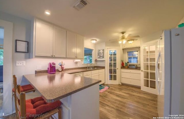 kitchen with white fridge with ice dispenser, a kitchen bar, kitchen peninsula, and white cabinetry