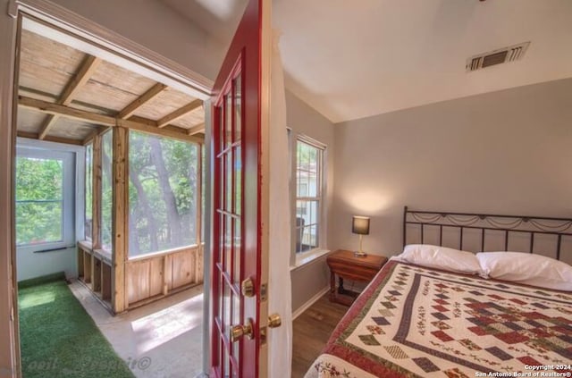 bedroom with lofted ceiling with beams, wood-type flooring, and multiple windows