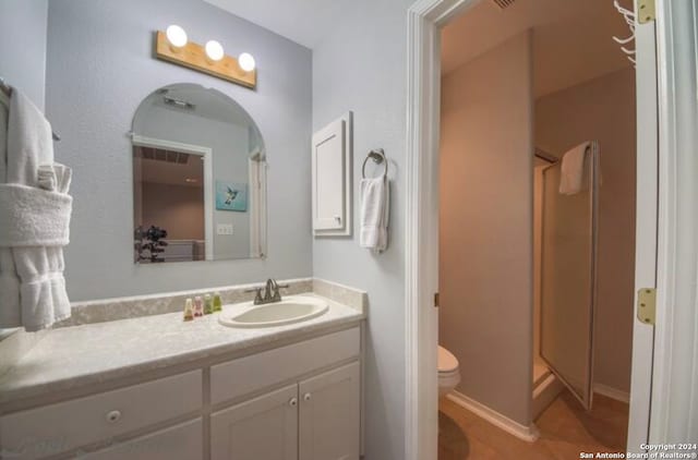 bathroom featuring tile patterned flooring, vanity, a shower with shower door, and toilet