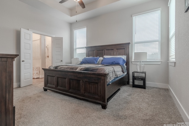 bedroom featuring ensuite bathroom, ceiling fan, light carpet, and a tray ceiling