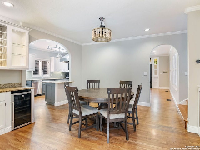 dining space featuring light wood-type flooring, crown molding, beverage cooler, and a chandelier