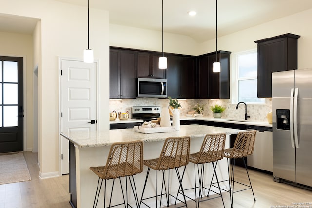 kitchen with a center island, sink, light stone countertops, light wood-type flooring, and appliances with stainless steel finishes