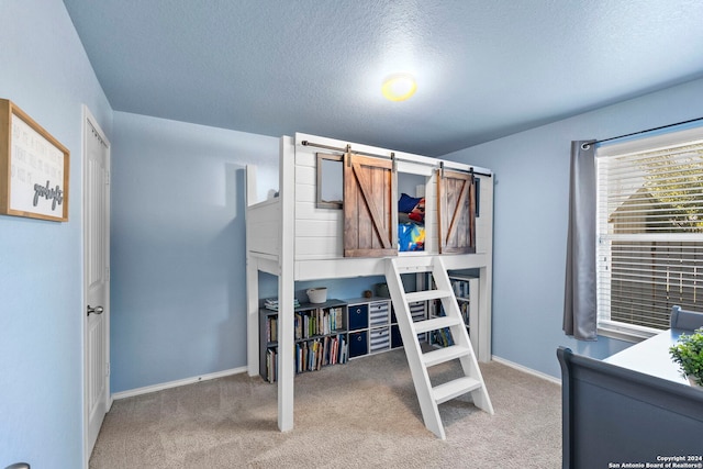 carpeted bedroom featuring a barn door and a textured ceiling