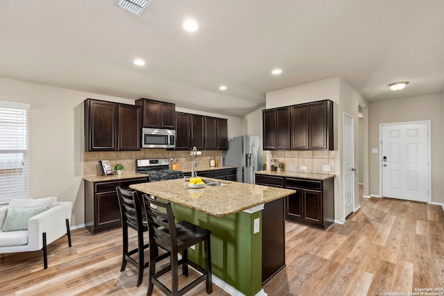 kitchen featuring a breakfast bar, a center island with sink, light hardwood / wood-style flooring, appliances with stainless steel finishes, and dark brown cabinets