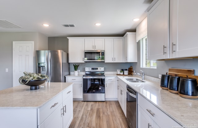 kitchen with white cabinetry, sink, light stone counters, light hardwood / wood-style floors, and appliances with stainless steel finishes