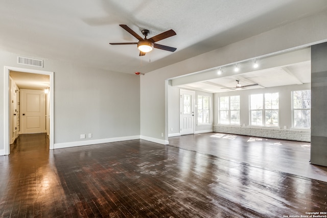 unfurnished living room featuring dark wood-type flooring, track lighting, ceiling fan, a textured ceiling, and beamed ceiling