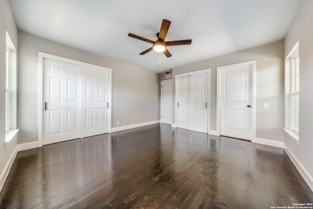 unfurnished bedroom with multiple closets, ceiling fan, and dark hardwood / wood-style flooring