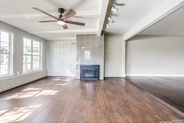 unfurnished living room featuring track lighting, brick wall, ceiling fan, beam ceiling, and hardwood / wood-style flooring