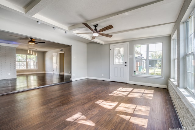 unfurnished living room featuring dark hardwood / wood-style floors, ceiling fan, a textured ceiling, beamed ceiling, and brick wall