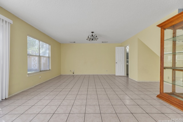 empty room with light tile patterned flooring, a textured ceiling, and a chandelier