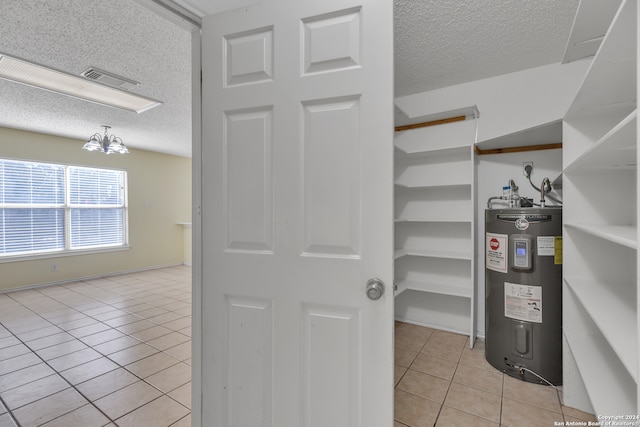 spacious closet with water heater, light tile patterned floors, and a notable chandelier