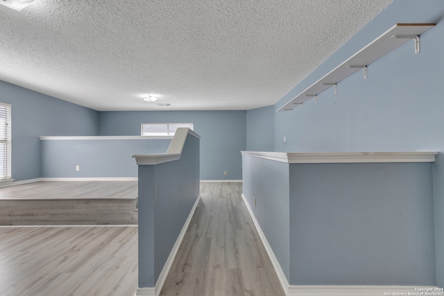 hall with light hardwood / wood-style floors and a textured ceiling