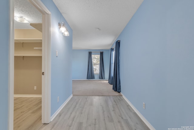 corridor with a textured ceiling and light wood-type flooring