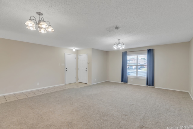 empty room with light carpet, a textured ceiling, and a notable chandelier