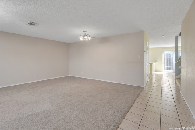 unfurnished room with light carpet, a textured ceiling, and a notable chandelier