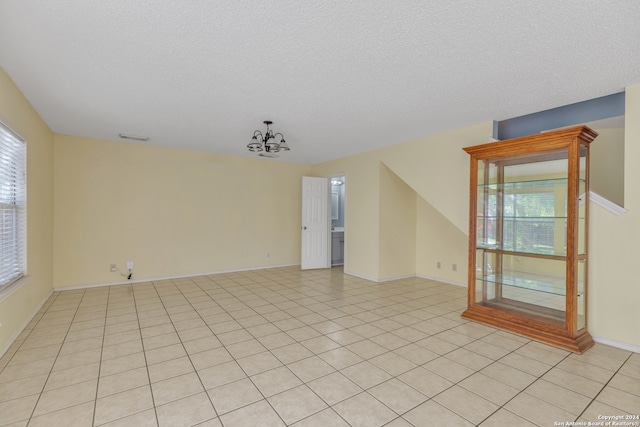 spare room with a notable chandelier, light tile patterned floors, and a textured ceiling