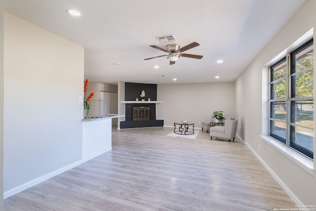 unfurnished room featuring ceiling fan, a fireplace, and light wood-type flooring