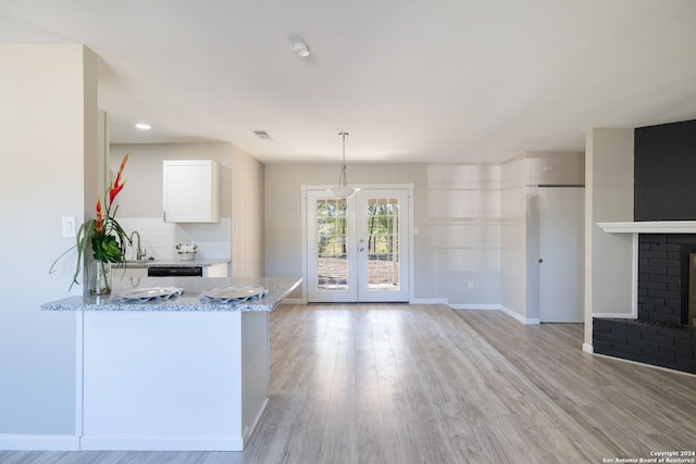 kitchen featuring kitchen peninsula, decorative backsplash, light stone countertops, decorative light fixtures, and white cabinetry