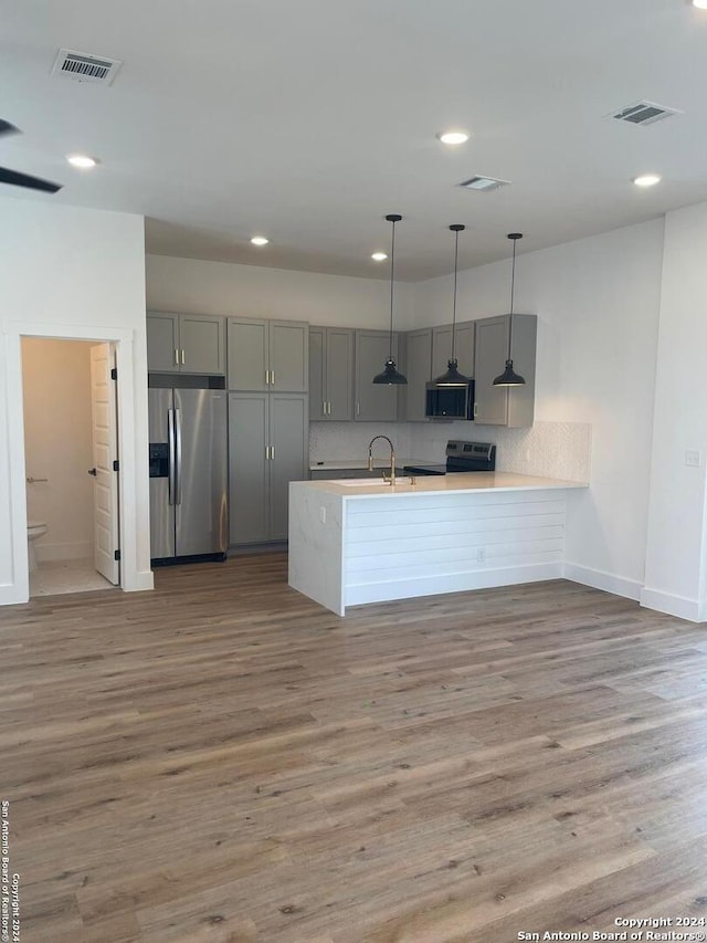 kitchen featuring kitchen peninsula, appliances with stainless steel finishes, sink, hardwood / wood-style flooring, and decorative light fixtures