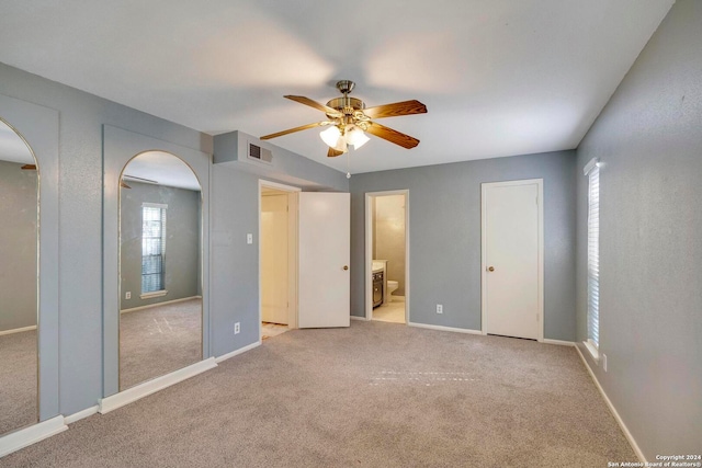 unfurnished bedroom with connected bathroom, light colored carpet, ceiling fan, and multiple closets